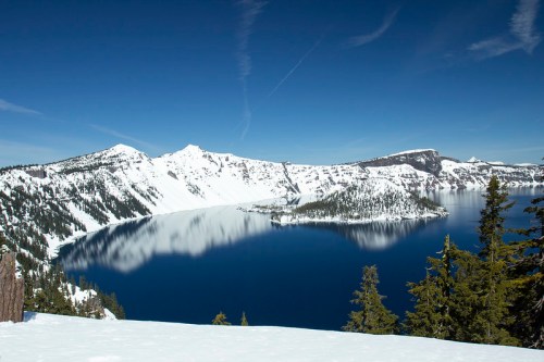 A stunning view of a snow-covered landscape surrounding a deep blue lake, with mountains reflecting in the water.