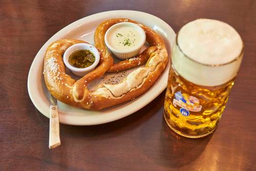 A large pretzel with dipping sauces on a plate, alongside a frothy beer in a glass.