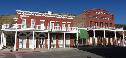 Historic buildings in Eureka, Utah, featuring the Opera House and a red-painted structure with a balcony. Clear blue sky.