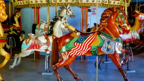 A colorful carousel featuring intricately painted horses, some adorned with flags and decorative designs.