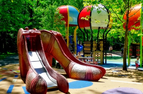 A whimsical playground featuring a large shoe-shaped slide surrounded by colorful play structures and trees.