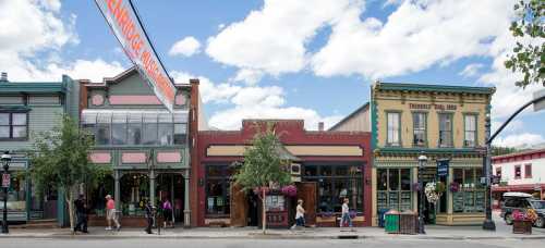 Colorful storefronts line a street under a blue sky with fluffy clouds, with people walking and enjoying the area.