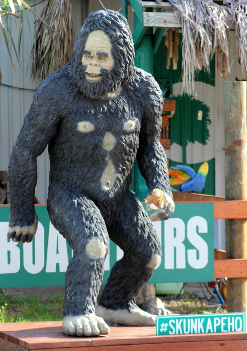 A large, detailed statue of Bigfoot stands on a wooden platform, surrounded by colorful signs and decorations.