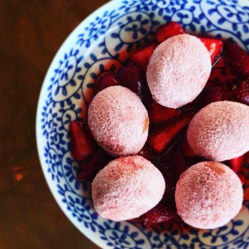 A blue and white bowl filled with fresh strawberries and round, pink mochi desserts.