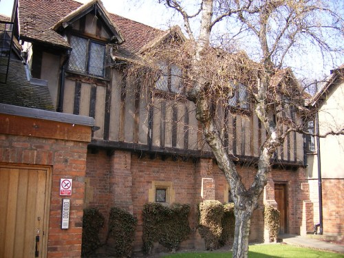 A historic building with timber framing and brick walls, featuring a tree in front and a well-maintained garden.