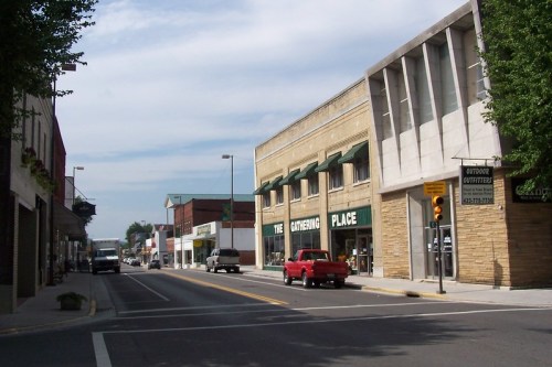 A street view featuring shops, a red truck, and a mix of modern and traditional buildings under a cloudy sky.