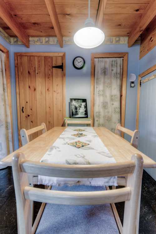 A cozy dining area with a wooden table, chairs, and a light fixture, featuring blue walls and wooden accents.