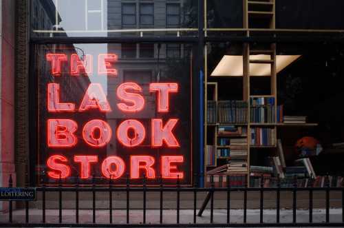 Neon sign reading "The Last Book Store" in a window, with bookshelves visible behind it.