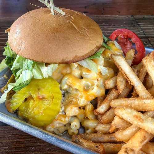 A burger topped with lettuce, cheese, and pickles, served with a side of crispy fries and a slice of tomato.