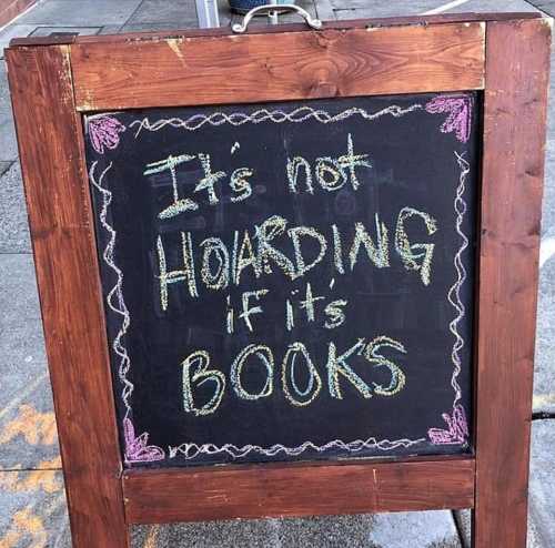 A chalkboard sign reads, "It's not HOARDING if it's BOOKS," with colorful decorations around the text.