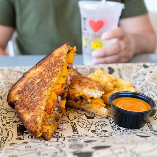 A grilled cheese sandwich with tomato and a side of macaroni, accompanied by a drink in a clear cup.