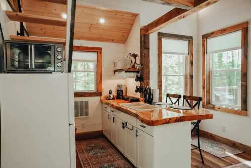 Cozy kitchen with wooden accents, white cabinets, a microwave, and large windows letting in natural light.