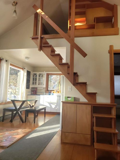 A cozy interior featuring a staircase, dining area, and kitchen with natural light and wooden accents.
