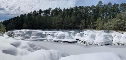 Snow-covered cliffs and a frozen lake, surrounded by evergreen trees under a cloudy sky.
