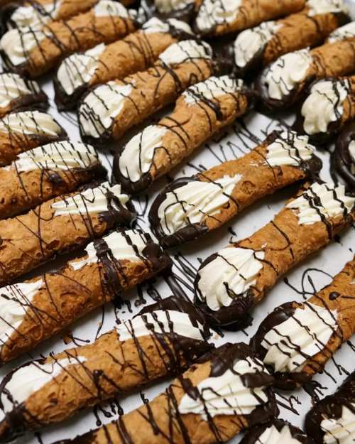 A close-up of neatly arranged cannoli filled with cream and drizzled with chocolate.