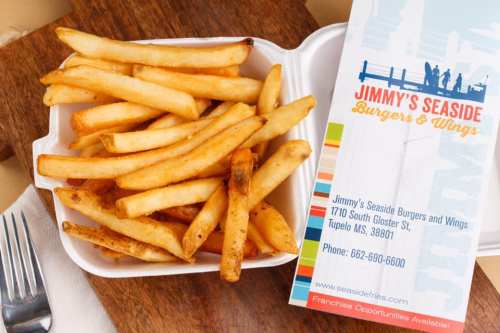 A takeout container filled with golden fries next to a menu from Jimmy's Seaside Burgers & Wings.