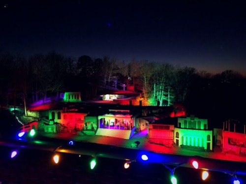 A colorful display of lights illuminates a hillside with structures, set against a darkening sky at dusk.