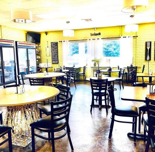 Bright, inviting restaurant interior with yellow walls, round tables, and black chairs, featuring large windows and a cozy atmosphere.