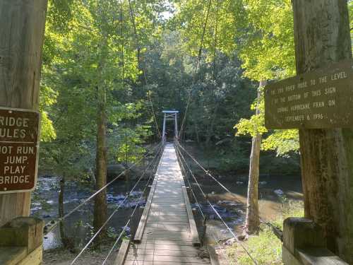 A suspension bridge surrounded by trees, with signs warning about flood levels and a historical note from 1996.