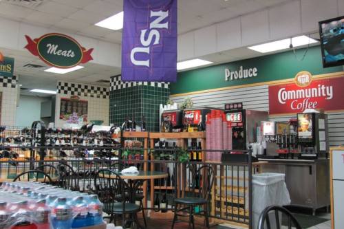 Interior of a grocery store featuring sections for meats and produce, with drink dispensers and tables for seating.