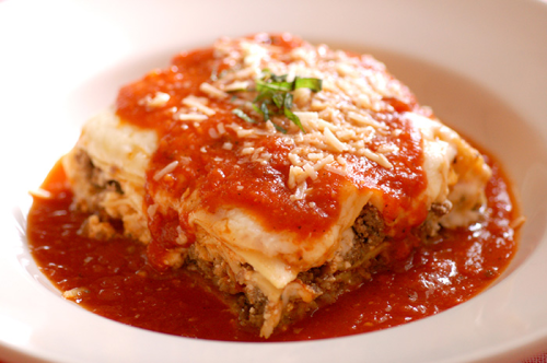 A serving of lasagna topped with marinara sauce and grated cheese, garnished with a sprig of basil.