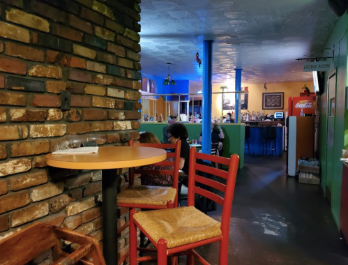 Cozy restaurant interior with brick walls, colorful lighting, and empty chairs at a small table.