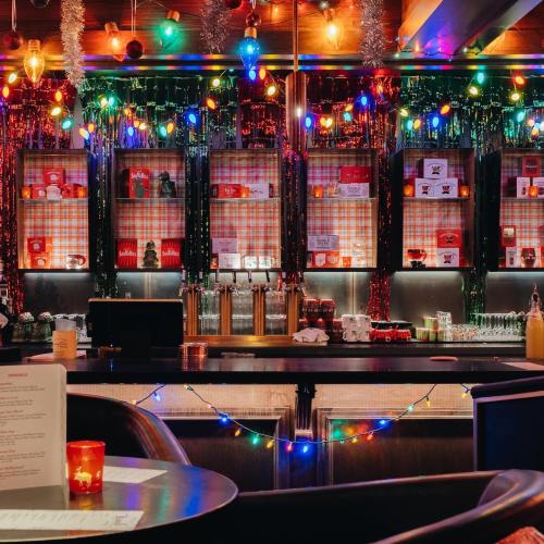 A festive bar with colorful lights, shimmering decorations, and shelves filled with drinks, creating a vibrant atmosphere.