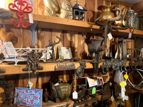 A wooden shelf filled with various vintage items, including tools, decor, and a sign for haircuts.
