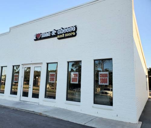 Exterior of a white building with large windows, featuring a sign for "mac & cheese and more" and "coming soon" notices.