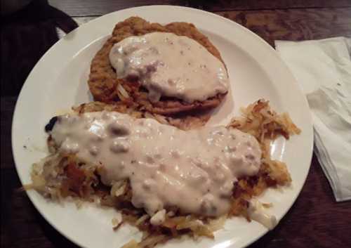 A plate with two fried patties topped with creamy gravy, served with a side of crispy hash browns.