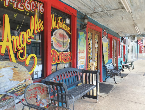Colorful storefront with vintage signs for "Angelle's Old Fashioned Burger," featuring benches and an American flag.