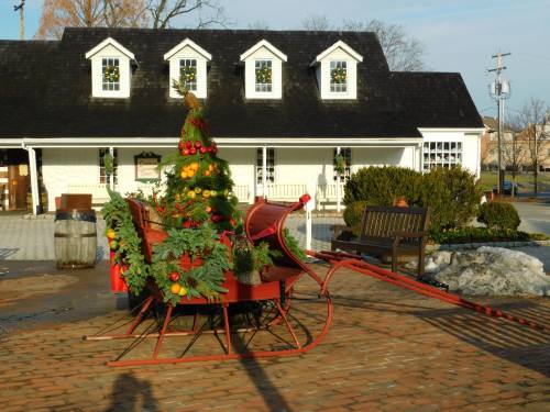 A festive sleigh decorated with greenery and fruits, set in front of a charming building with holiday decorations.