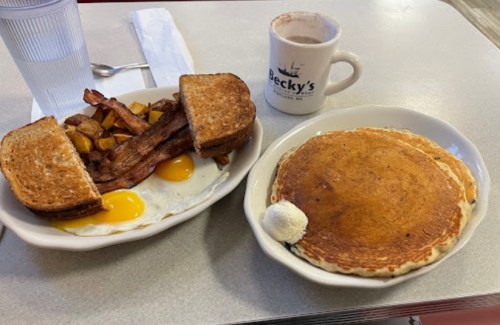 A breakfast plate with eggs, bacon, toast, and pancakes with butter, alongside a cup of coffee at a diner.