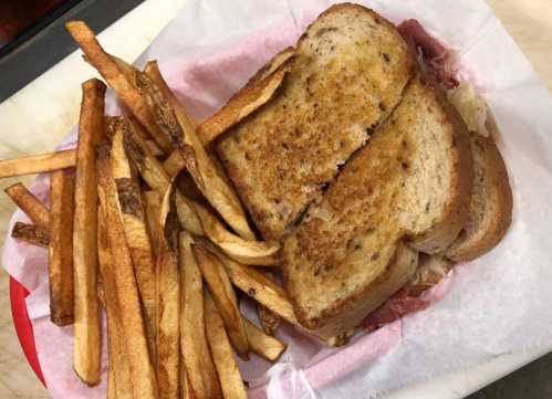 A grilled sandwich with golden-brown bread served alongside crispy French fries on a red plate.