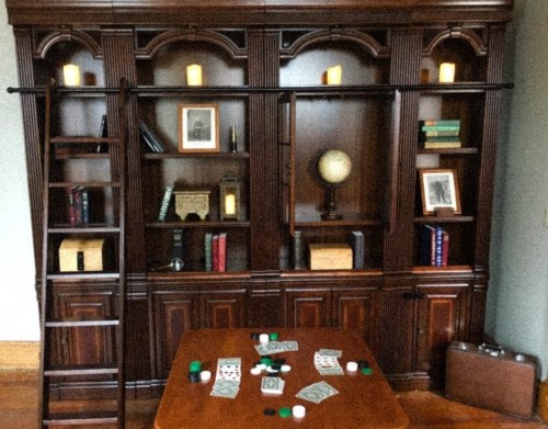 A wooden bookshelf with a ladder, featuring books, a globe, and a table with poker chips and playing cards.