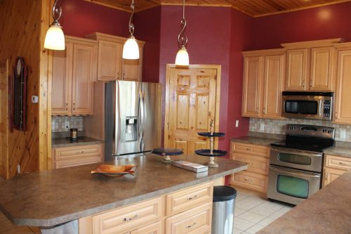A modern kitchen with wooden cabinets, stainless steel appliances, and a spacious island with pendant lighting.