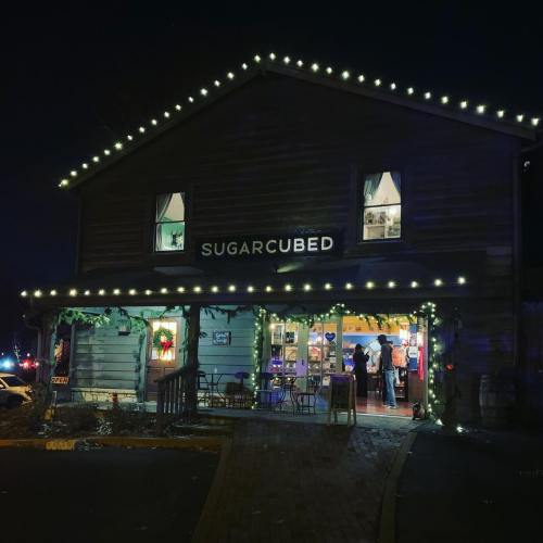A cozy shop named "Sugarcubed" adorned with festive lights, open at night with people inside.