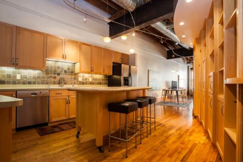 Modern kitchen with wooden cabinets, stainless steel appliances, and a central island with bar stools. Bright and spacious design.