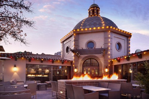 A beautifully lit outdoor dining area with a dome structure, surrounded by fire features and festive decorations.