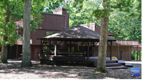 A modern wooden house surrounded by trees, featuring a gazebo and a spacious deck.