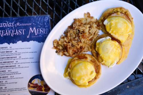 A plate of eggs Benedict with hash browns, next to a breakfast menu on a table.