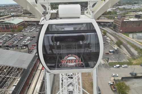 A close-up of a gondola on the St. Louis Wheel, with a view of the city and parking lot below.