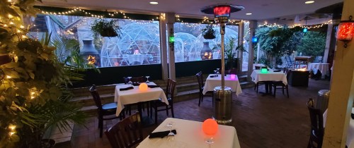 Cozy restaurant interior with tables, ambient lighting, and outdoor views of greenery and decorative elements.