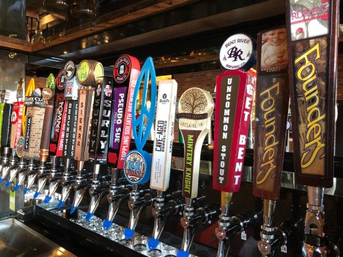 A row of colorful beer taps featuring various brewery logos and beer names in a bar setting.