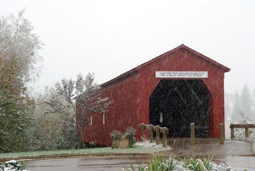 A red covered bridge in a snowy landscape, with a sign indicating a fine for driving through.