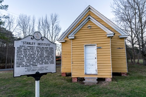 Historic yellow building with a sign reading "Stanley Institute," surrounded by trees and grass.