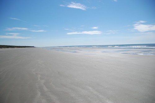 A serene beach scene with smooth sand, gentle waves, and a clear blue sky.