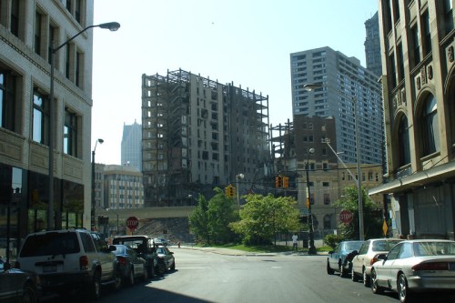 Urban scene showing a partially demolished building with surrounding cars and city structures in the background.