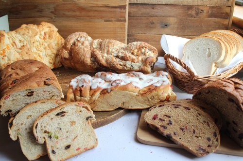 A variety of breads displayed on a wooden surface, including loaves, rolls, and sliced bread with different textures and colors.