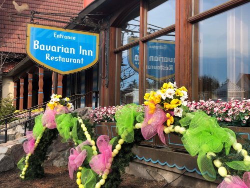 Sign for Bavarian Inn Restaurant with colorful floral decorations and greenery at the entrance.